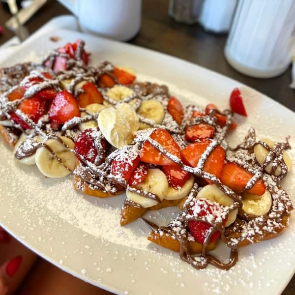 Waffles topped with sliced strawberries, bananas, chocolate drizzle, and powdered sugar at Route 12 Cafe.