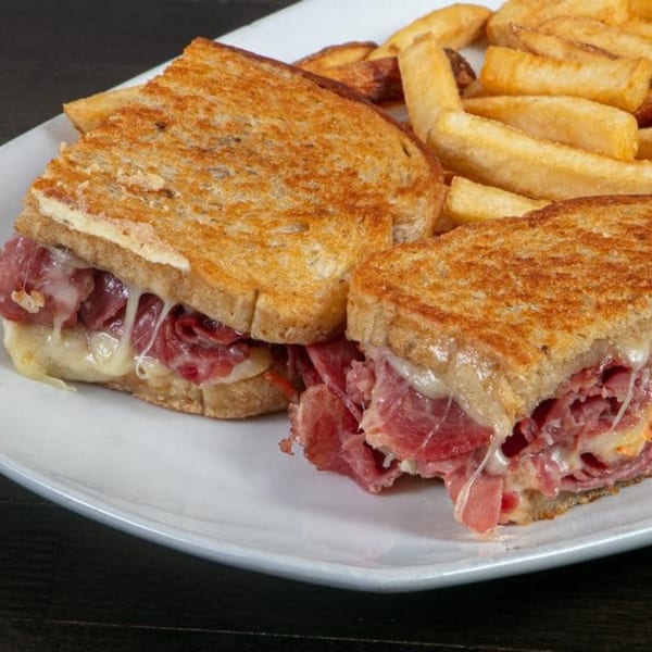 A grilled sandwich with melted cheese and deli meat, served with a side of golden french fries.