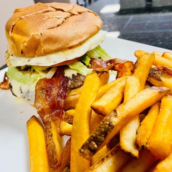 A breakfast burger with egg, bacon, lettuce, and cheese, served with a side of fries.