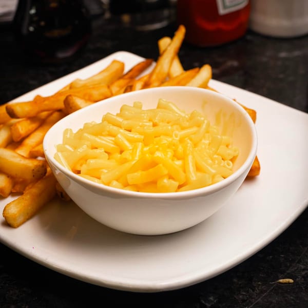 A white bowl of macaroni and cheese sits on a white plate with golden french fries.